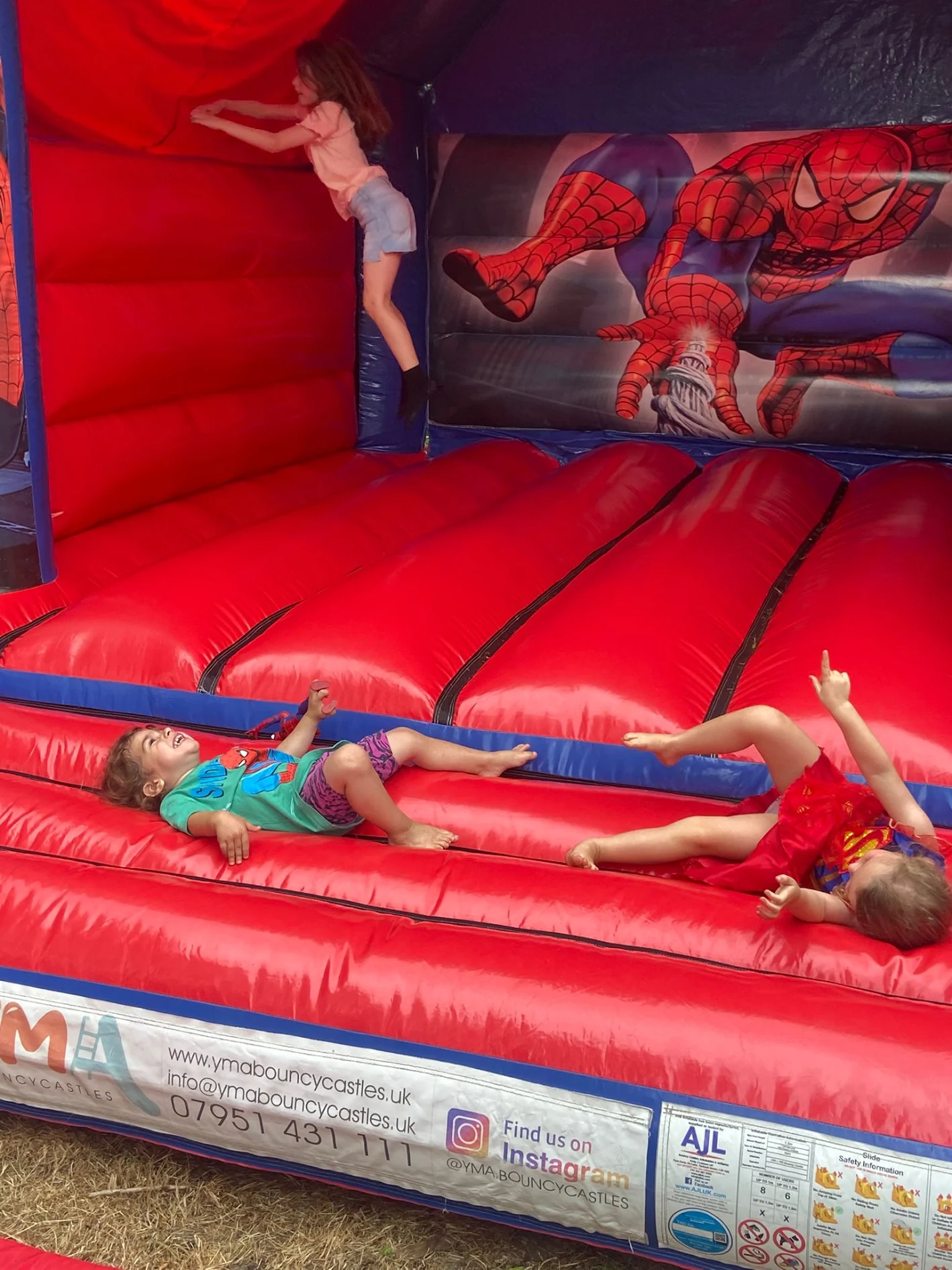 Happy children bouncing on a red Spiderman themed bouncy castle.